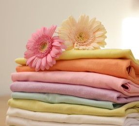 Photo of Stack of clean clothes and flowers on wooden table