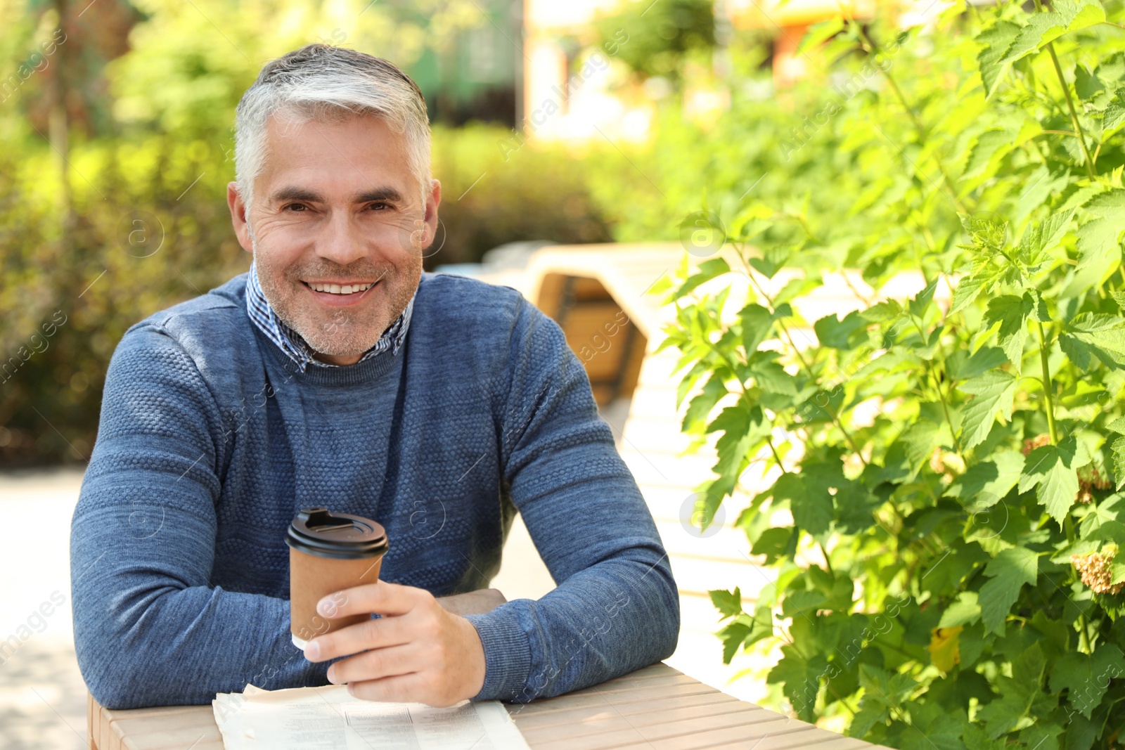 Photo of Handsome mature man sitting at table in park. Space for text