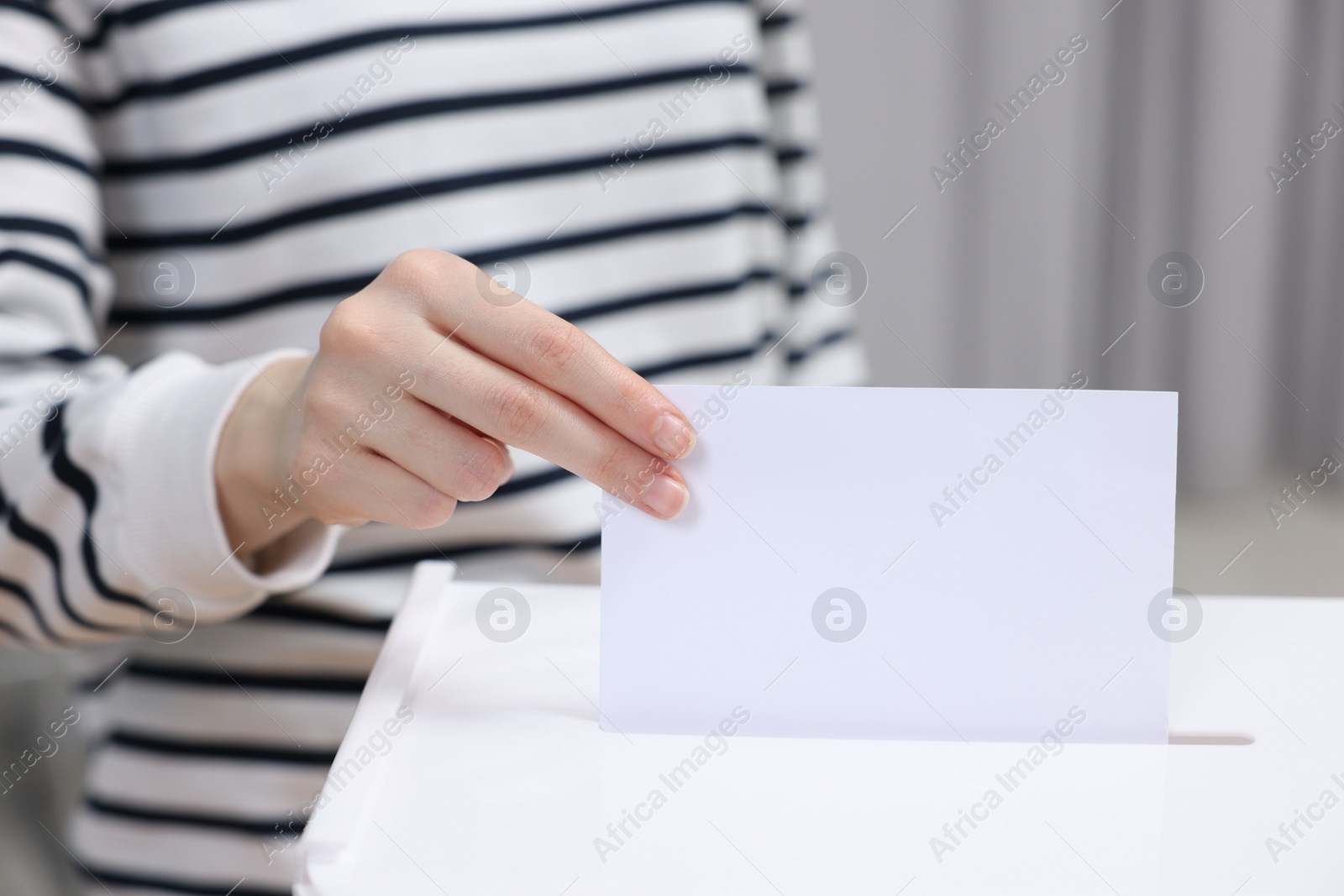 Photo of Woman putting her vote into ballot box on blurred background, closeup