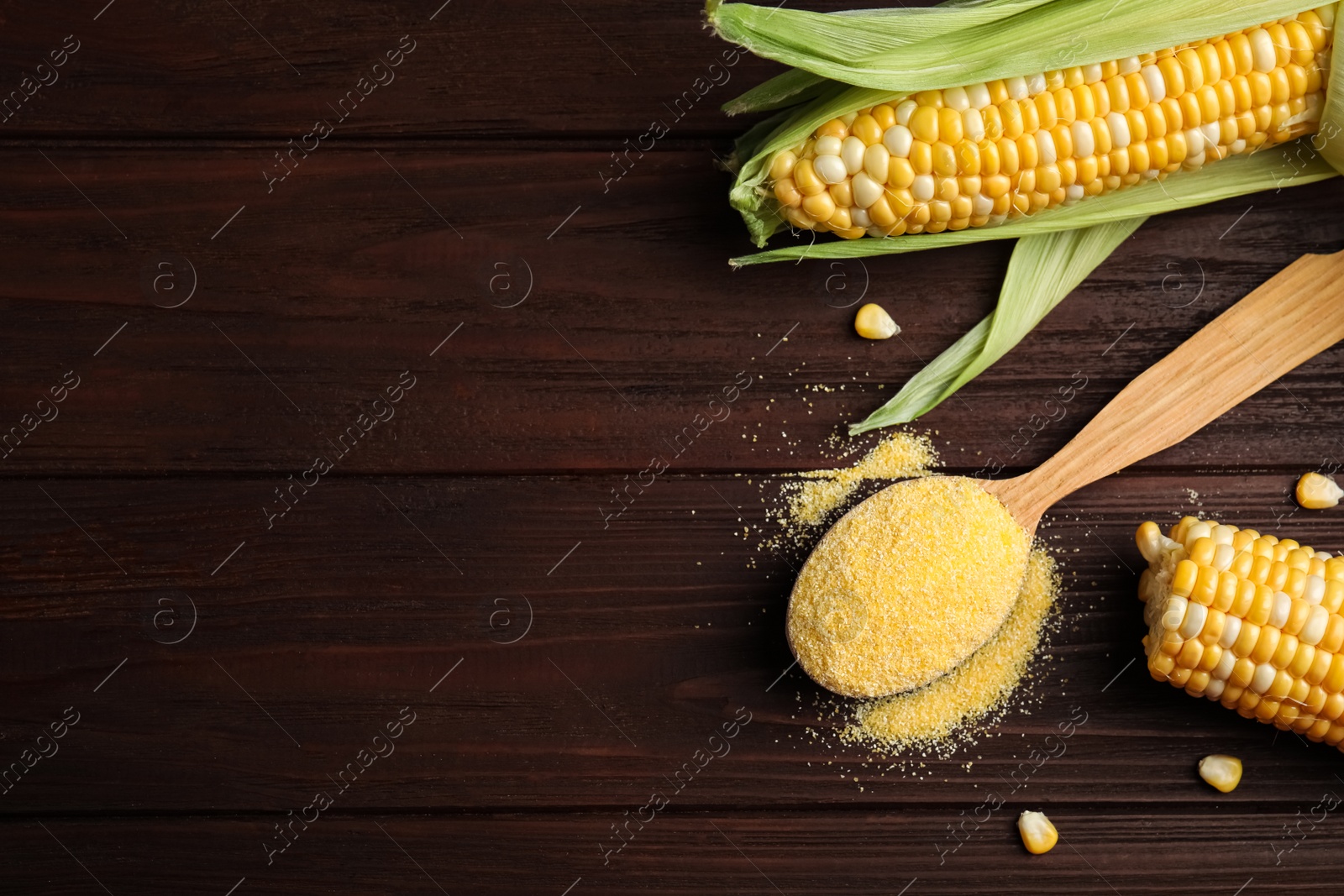 Photo of Cornmeal in spoon and fresh cobs on wooden table, flat lay. Space for text