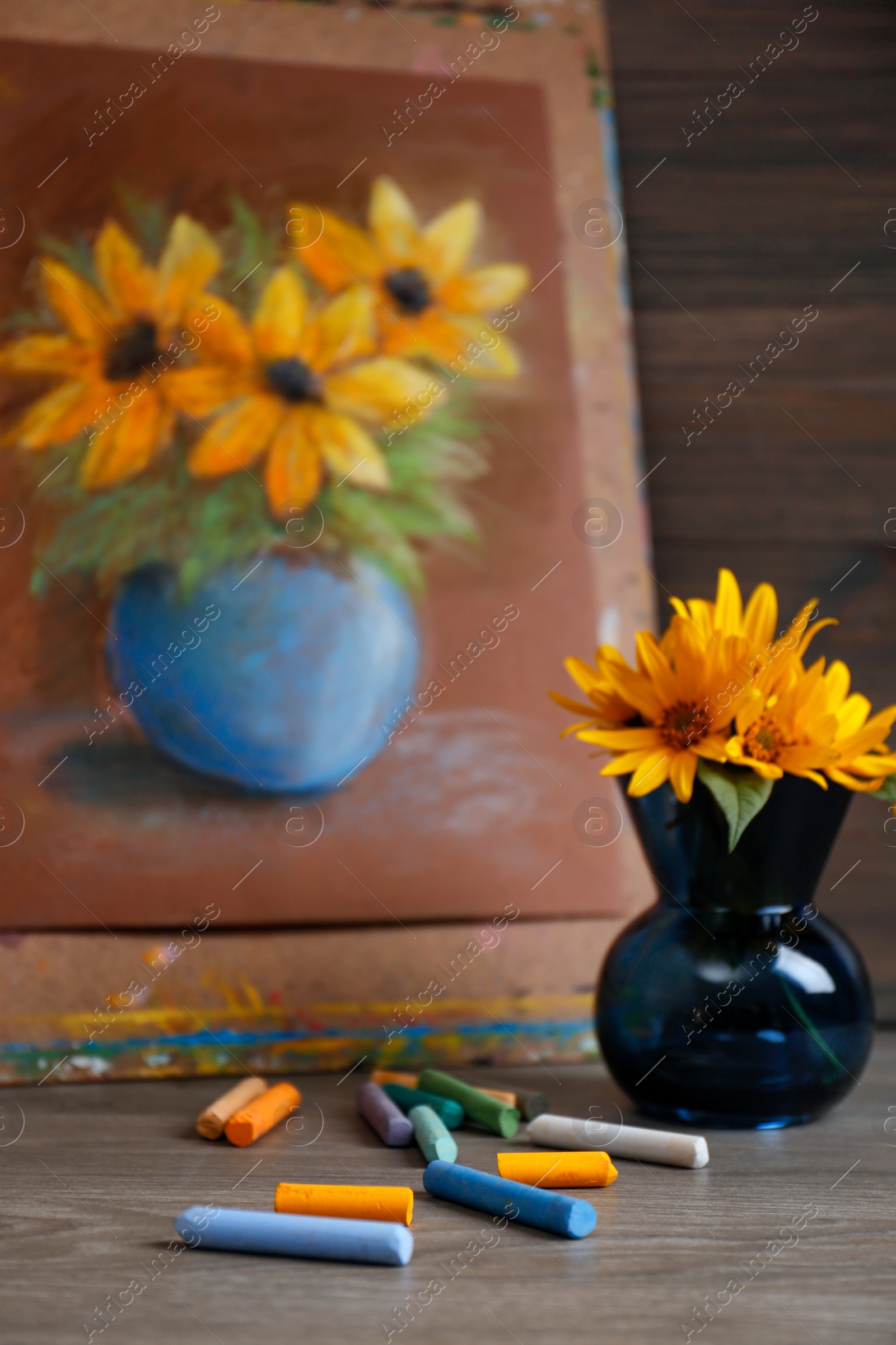 Photo of Yellow flowers, beautiful drawing and set of colorful pastels on wooden table