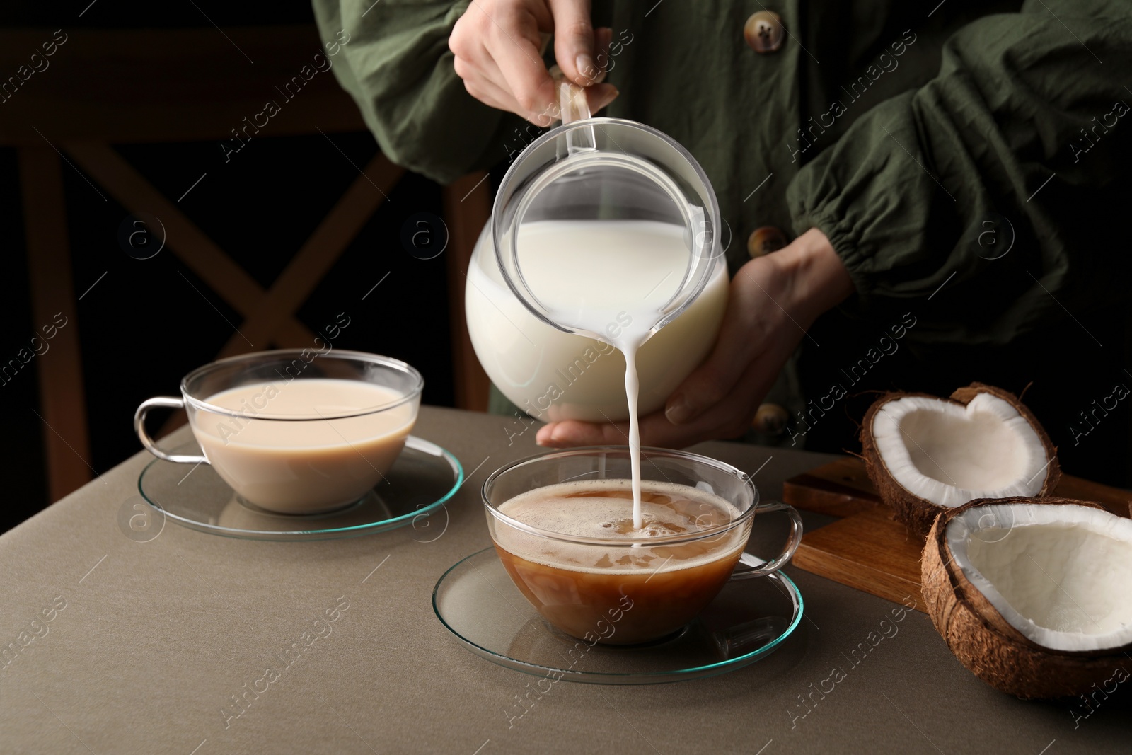 Photo of Woman pouring tasty coconut milk into cup of coffee at table, closeup