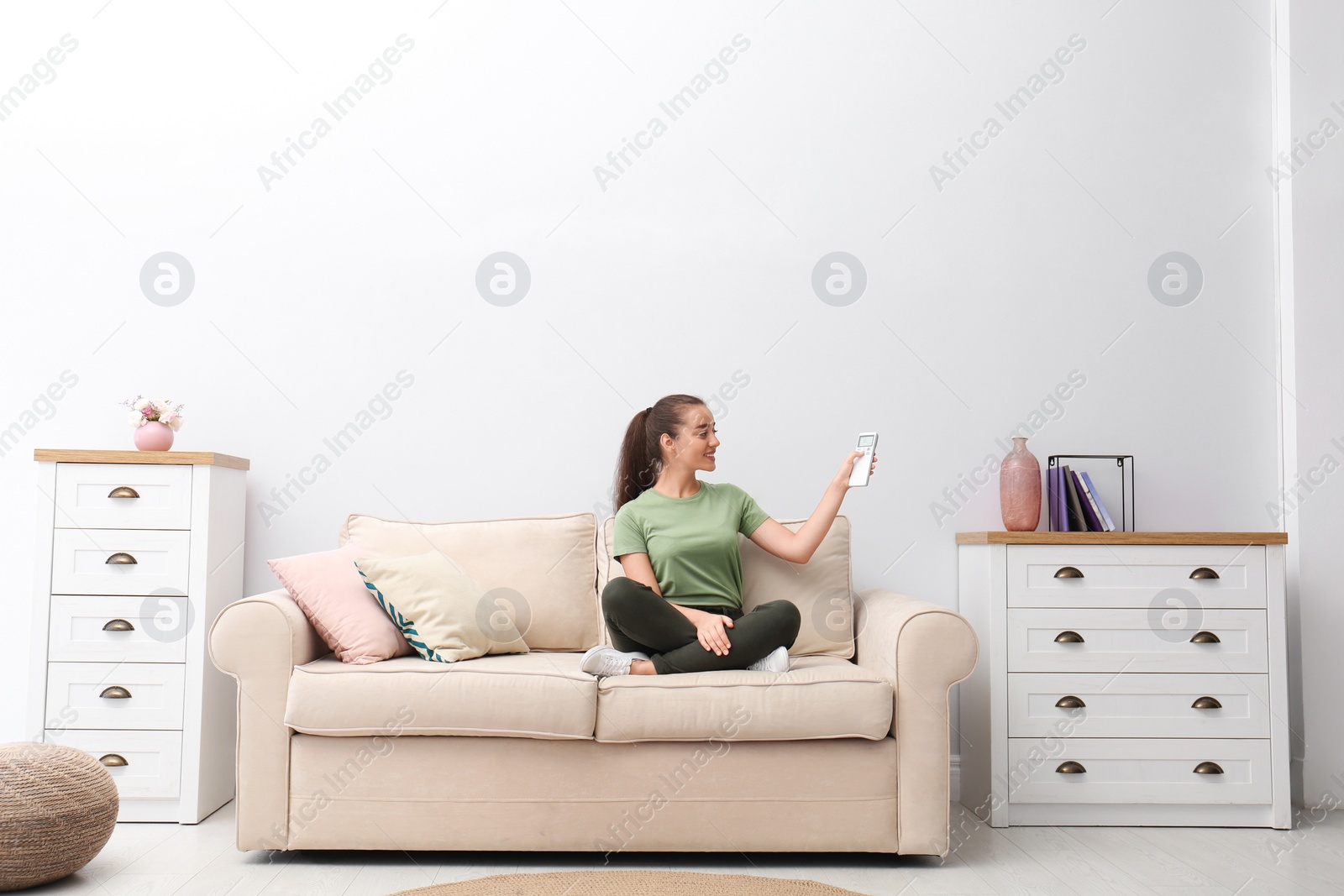 Photo of Happy young woman switching on air conditioner with remote control at home