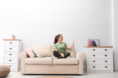 Photo of Happy young woman switching on air conditioner with remote control at home