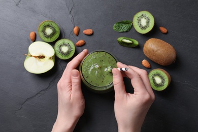 Photo of Woman with delicious kiwi smoothie and ingredients at black table, top view