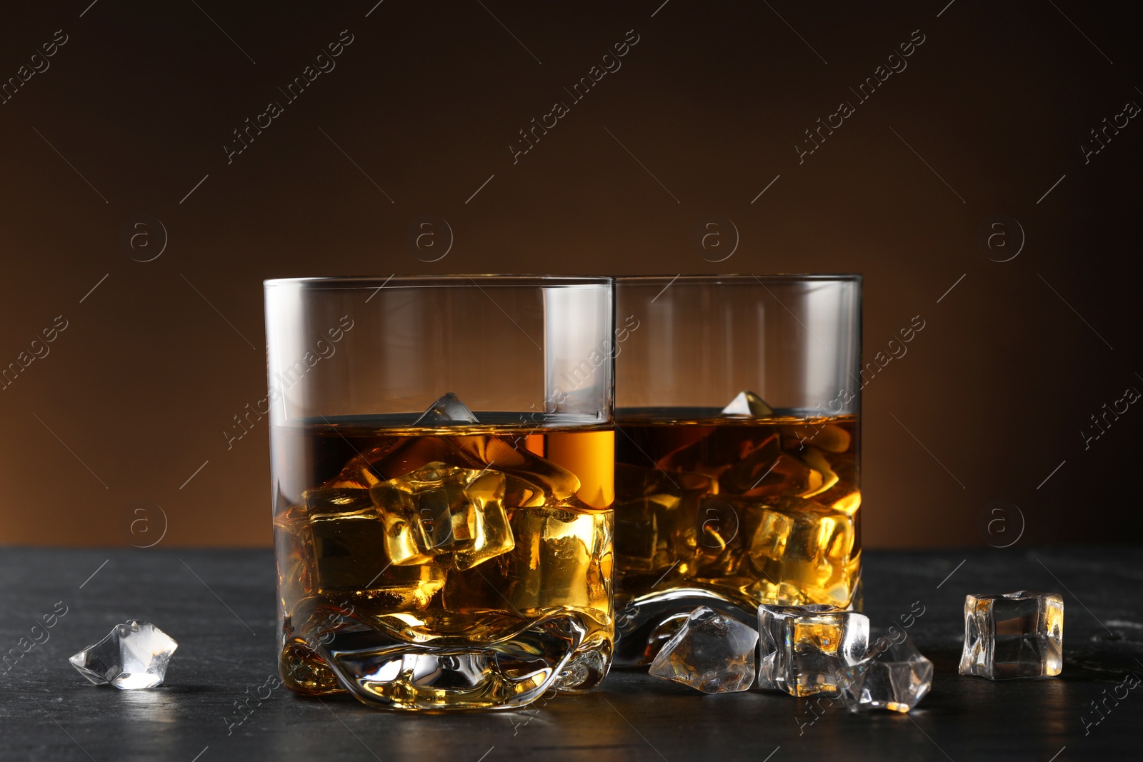 Photo of Whiskey and ice cubes in glasses on black table, closeup