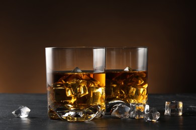 Photo of Whiskey and ice cubes in glasses on black table, closeup