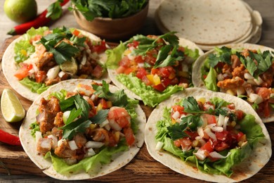 Delicious tacos with vegetables, meat and lime on table, closeup