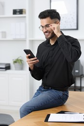 Photo of Happy young man using smartphone in office