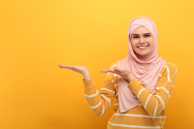 Muslim woman in hijab pointing at something on orange background