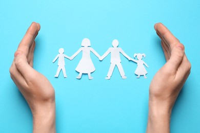 Woman protecting paper cutout of family on light blue background, top view