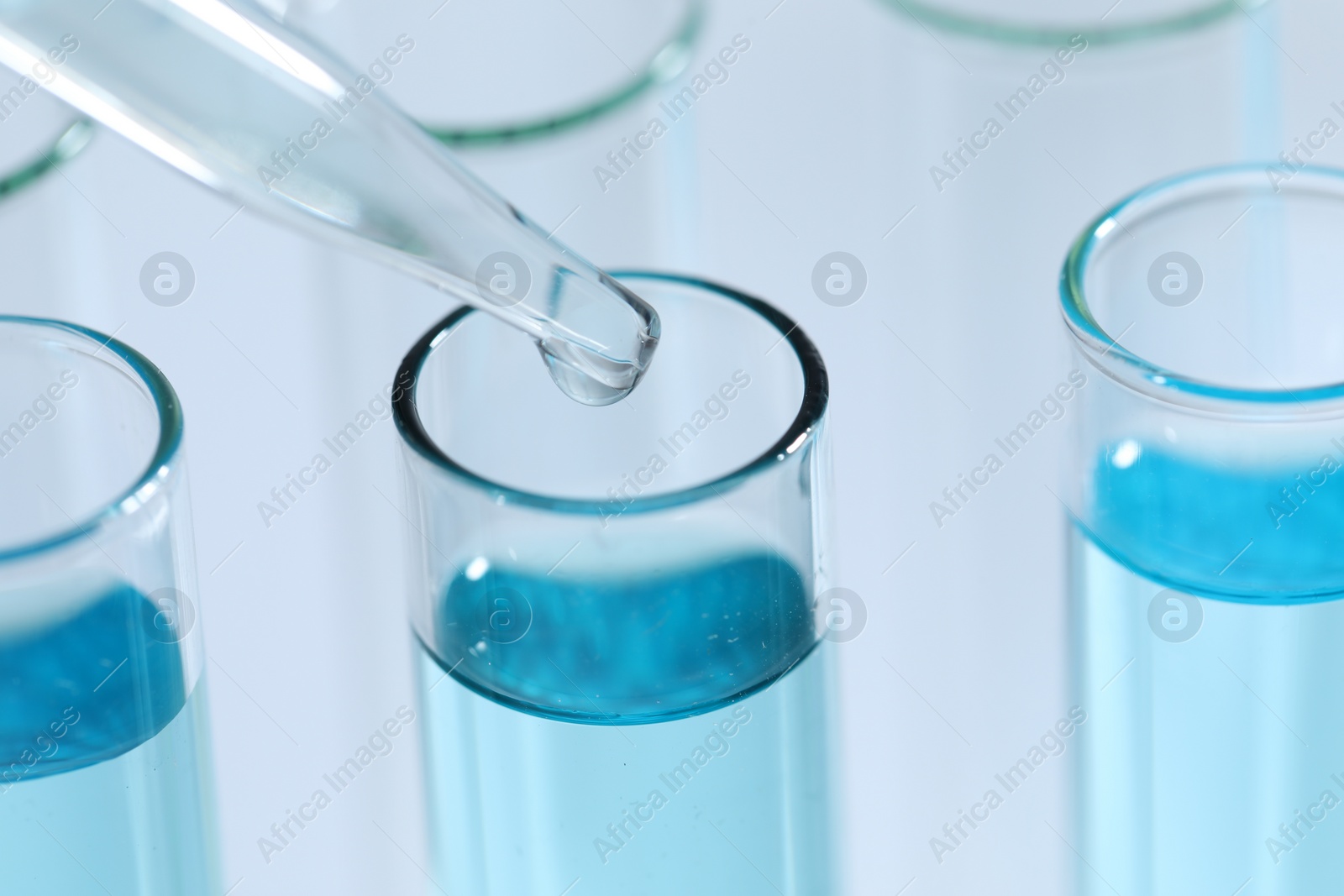 Photo of Dripping liquid from pipette into test tube on light background, closeup