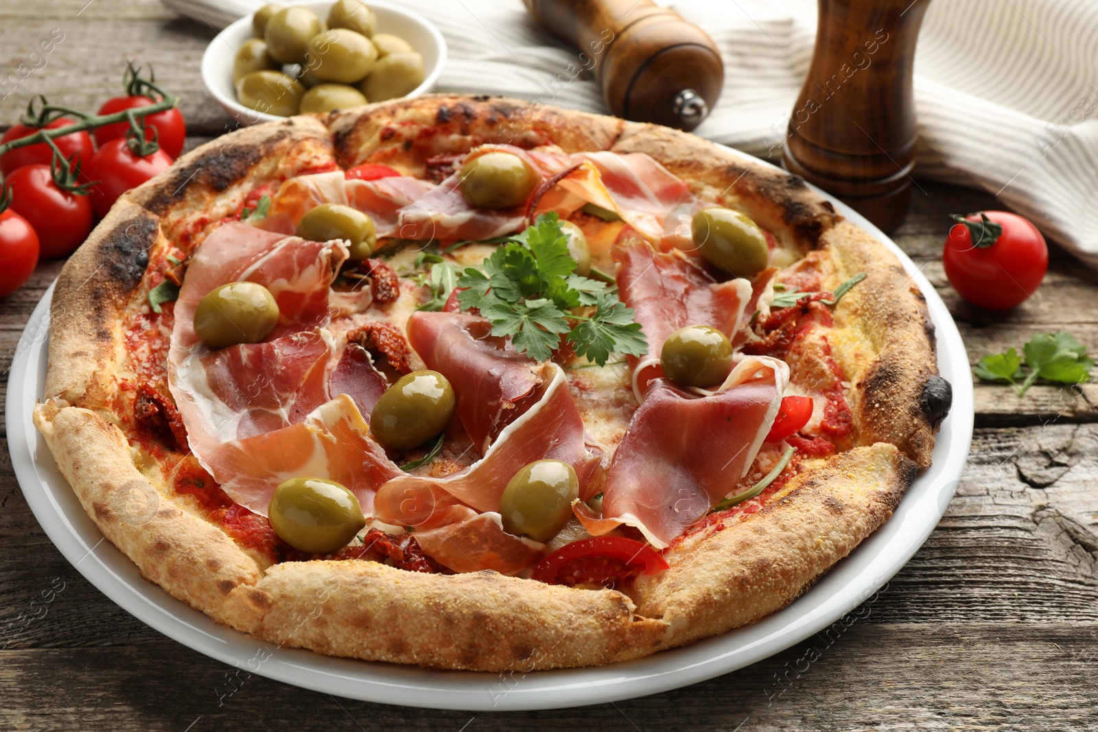 Photo of Tasty pizza with cured ham, olives, tomatoes and parsley on wooden table