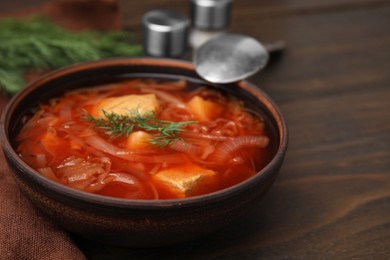 Photo of Bowl of delicious borscht on wooden table, closeup. Space for text