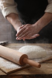 Photo of Man sprinkling flour over dough at wooden table, closeup