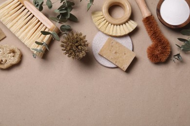 Photo of Cleaning brushes, baking soda, soap, loofah and eucalyptus leaves on pale brown background, flat lay. Space for text