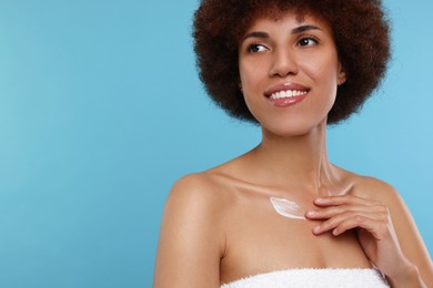 Photo of Beautiful young woman applying cream onto body on light blue background, space for text