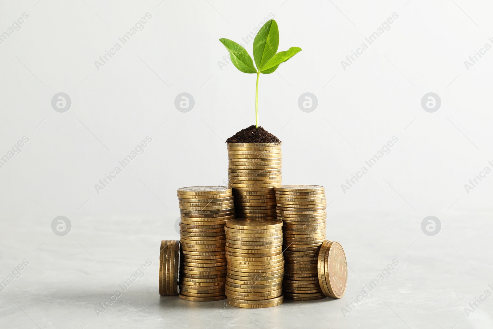 Photo of Stacked coins and green sprout on white marble table. Investment concept