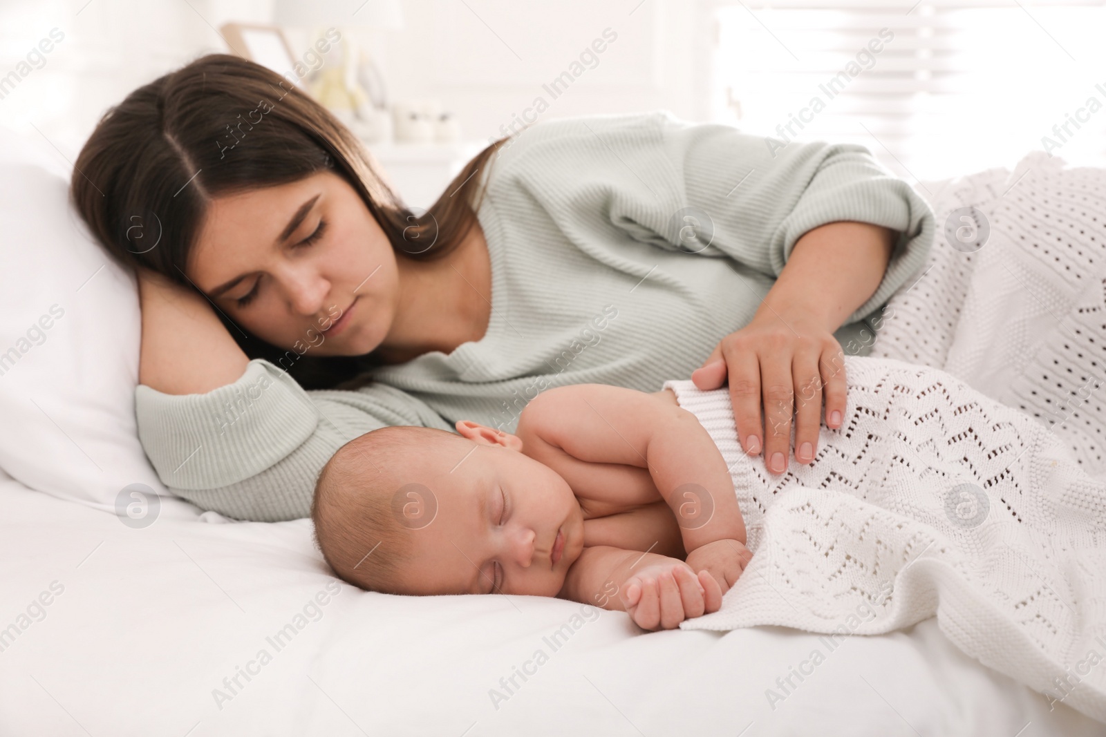 Photo of Young mother resting near her sleeping baby on bed at home