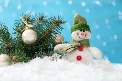 Cute toy snowman and fir branch decorated with Christmas balls on snow against blurred background