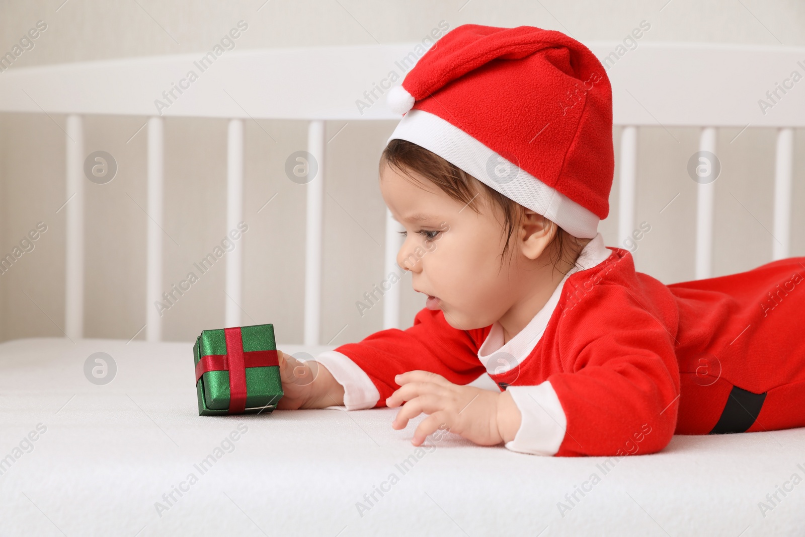 Photo of Cute baby wearing festive Christmas costume with gift box in crib