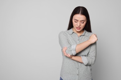 Photo of Young woman suffering from pain in elbow on light grey background, space for text. Arthritis symptoms