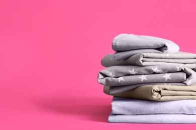 Photo of Stack of clean bed sheets on pink background. Space for text