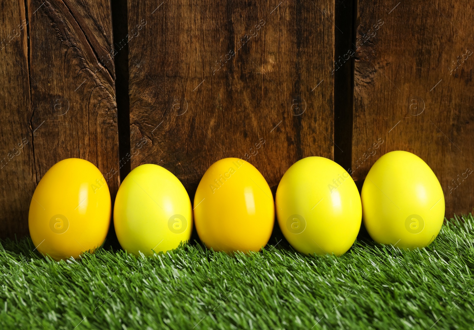 Photo of Bright Easter eggs on green grass against wooden background