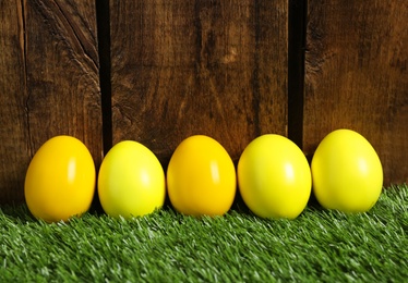 Bright Easter eggs on green grass against wooden background
