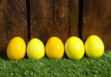 Photo of Bright Easter eggs on green grass against wooden background