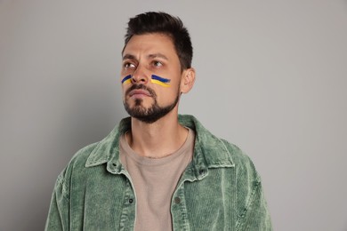 Photo of Man with drawings of Ukrainian flag on face against light grey background