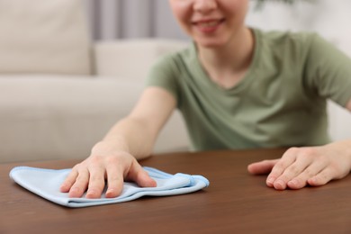 Photo of Woman with microfiber cloth cleaning wooden table in room, closeup
