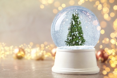 Image of Snow globe with Christmas tree on marble table, space for text. Bokeh effect