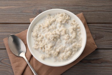 Photo of Tasty boiled oatmeal in bowl and spoon on wooden table, top view