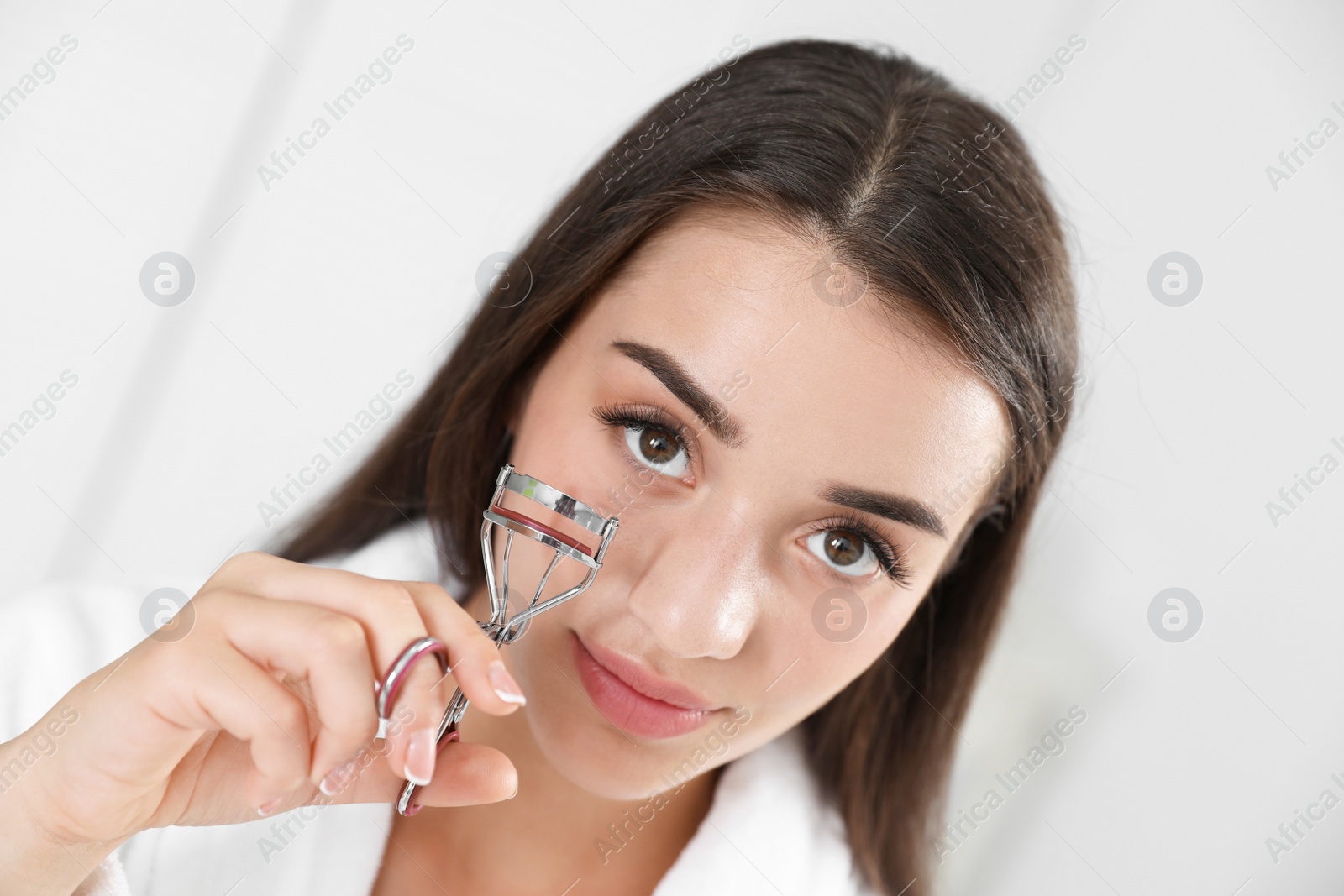 Photo of Attractive young woman with eyelash curler indoors