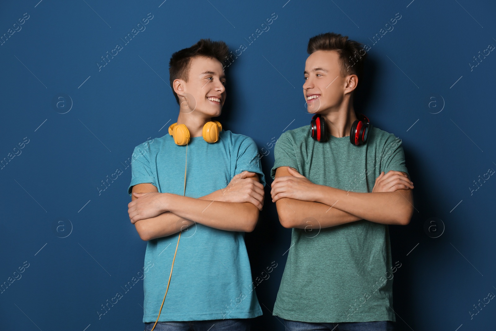 Photo of Teenage twin brothers with headphones on color background