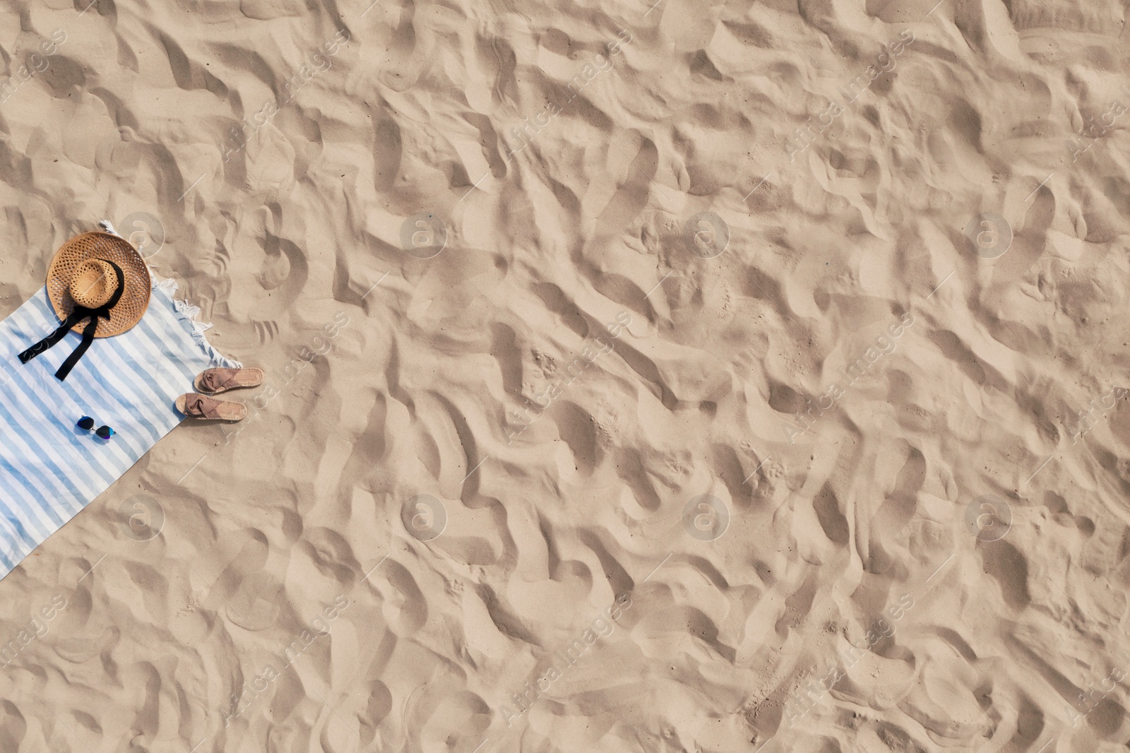 Image of Towel with beach accessories on sand, top view. Space for text