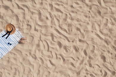 Towel with beach accessories on sand, top view. Space for text