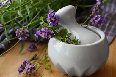 Photo of Mortar with fresh lavender flowers, green twigs and pestle on wooden table