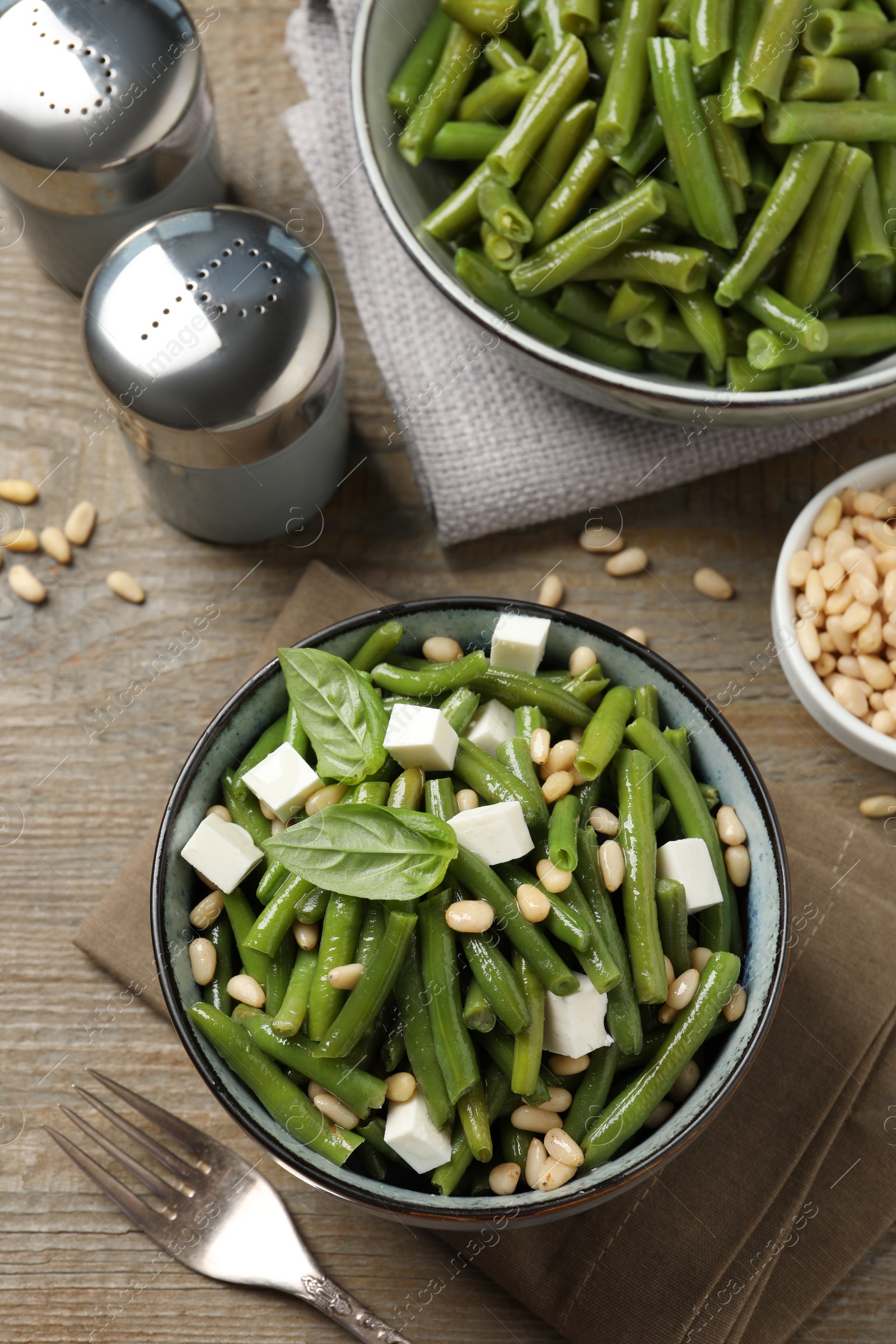 Photo of Delicious salad with green beans, pine nuts and cheese served on wooden table, flat lay