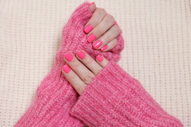 Woman showing her manicured hands with pink nail polish on knitted blanket, top view