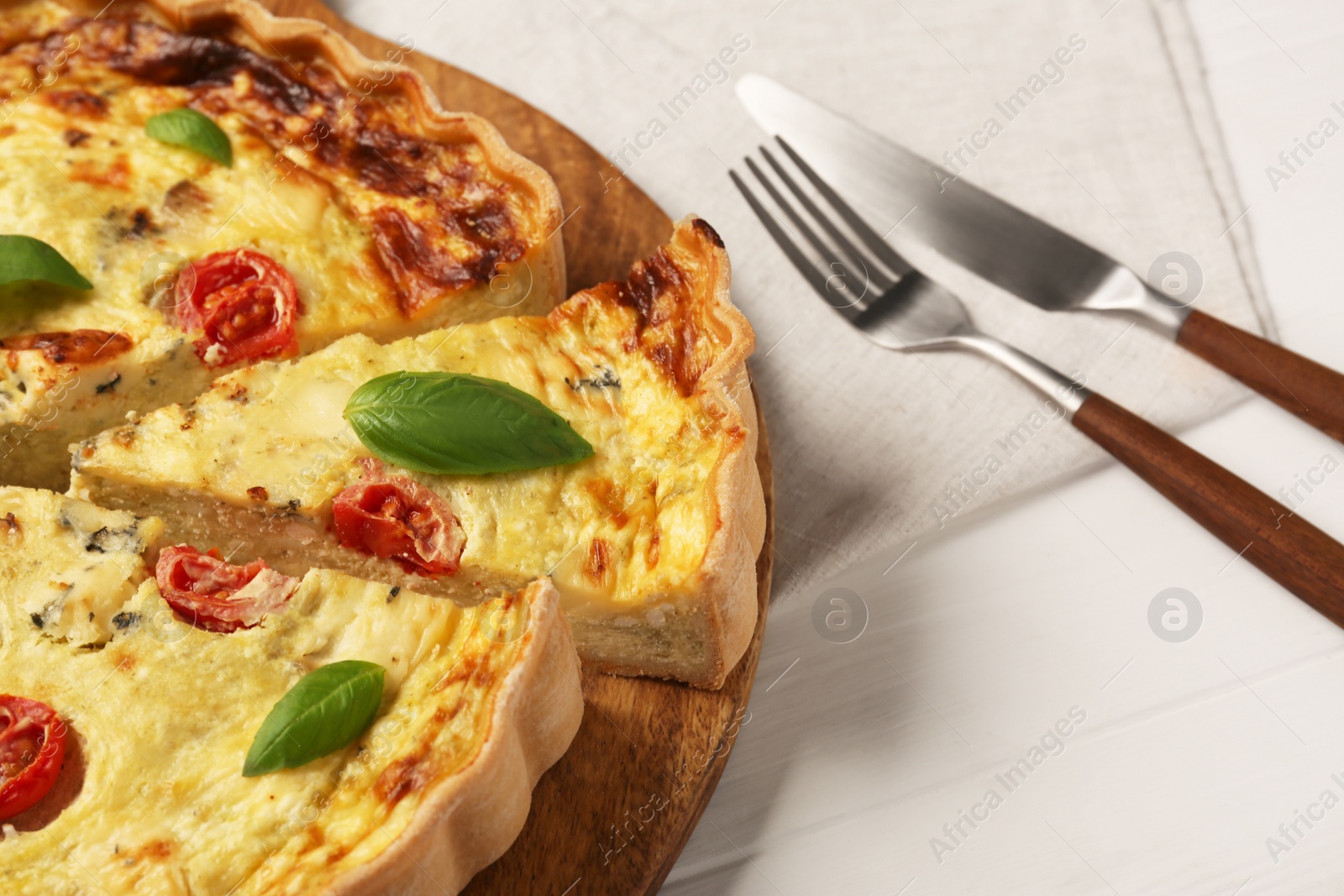 Photo of Delicious homemade cheese quiche and cutlery on white wooden table, closeup