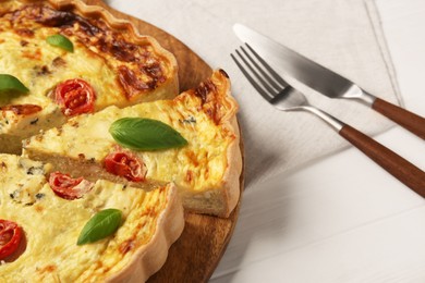 Photo of Delicious homemade cheese quiche and cutlery on white wooden table, closeup