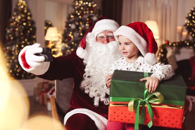Santa Claus and little girl taking selfie in room decorated for Christmas