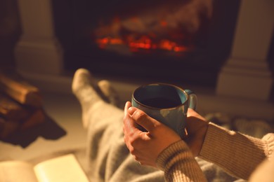 Photo of Woman with cup of hot drink resting near fireplace at home, closeup. Space for text