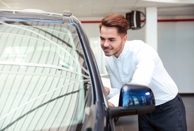 Young man near new car in dealership