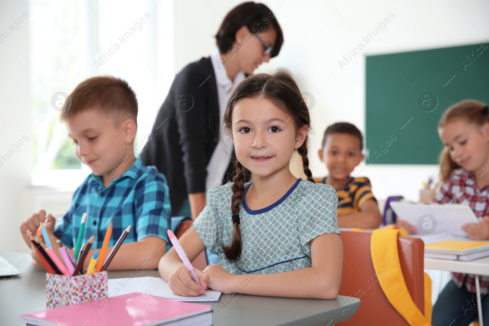 Photo of Adorable little children sitting at desks in classroom. Elementary school