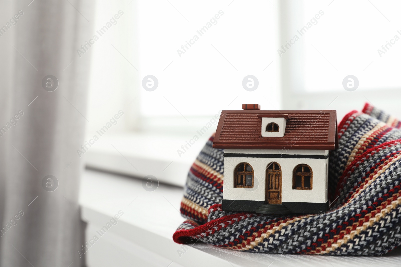 Photo of House model and scarf on window sill indoors, space for text. Heating efficiency