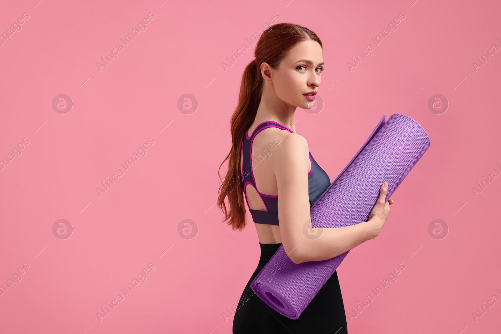 Photo of Woman in sportswear with fitness mat on pink background, space for text