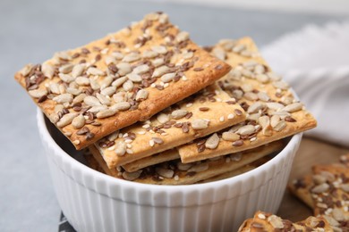 Photo of Cereal crackers with flax, sunflower and sesame seeds in bowl on grey table, closeup